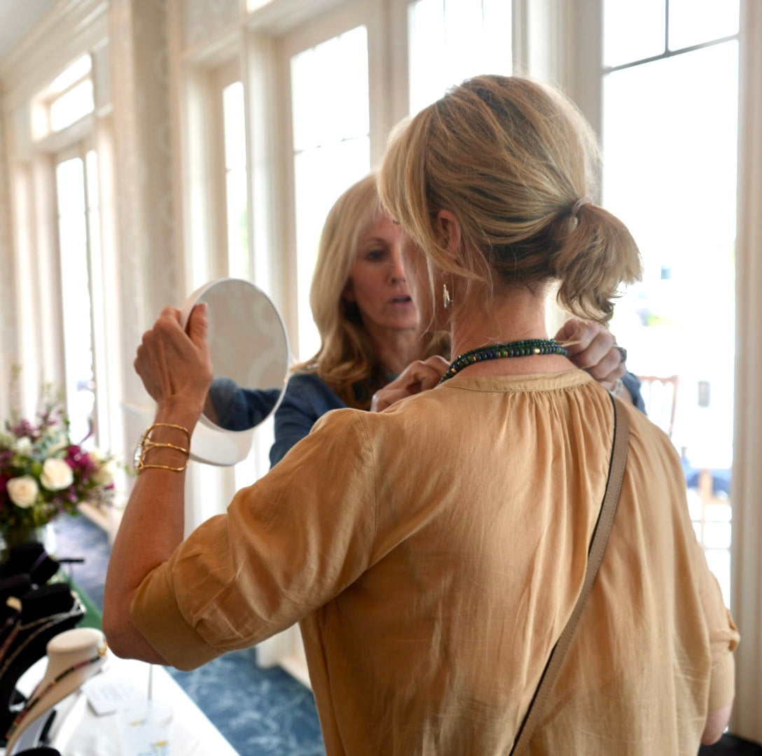 Woman trying on a MariaRyan Jewelry necklace and looking in the mirror. 