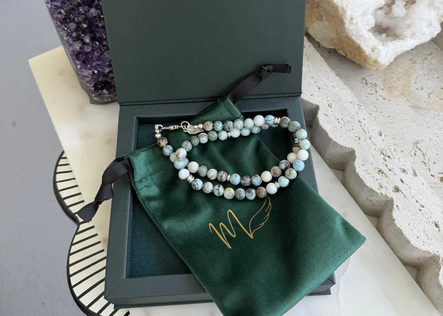 Necklace on a green cloth jewelry bag on an open green jewelry box, with crystals in the background.