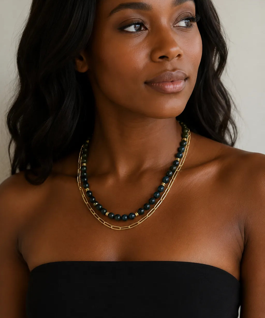 A woman wearing layered necklaces by MariaRyan Jewelry. One has ronud dark teal apitie beads and the other has gold paperclip links.