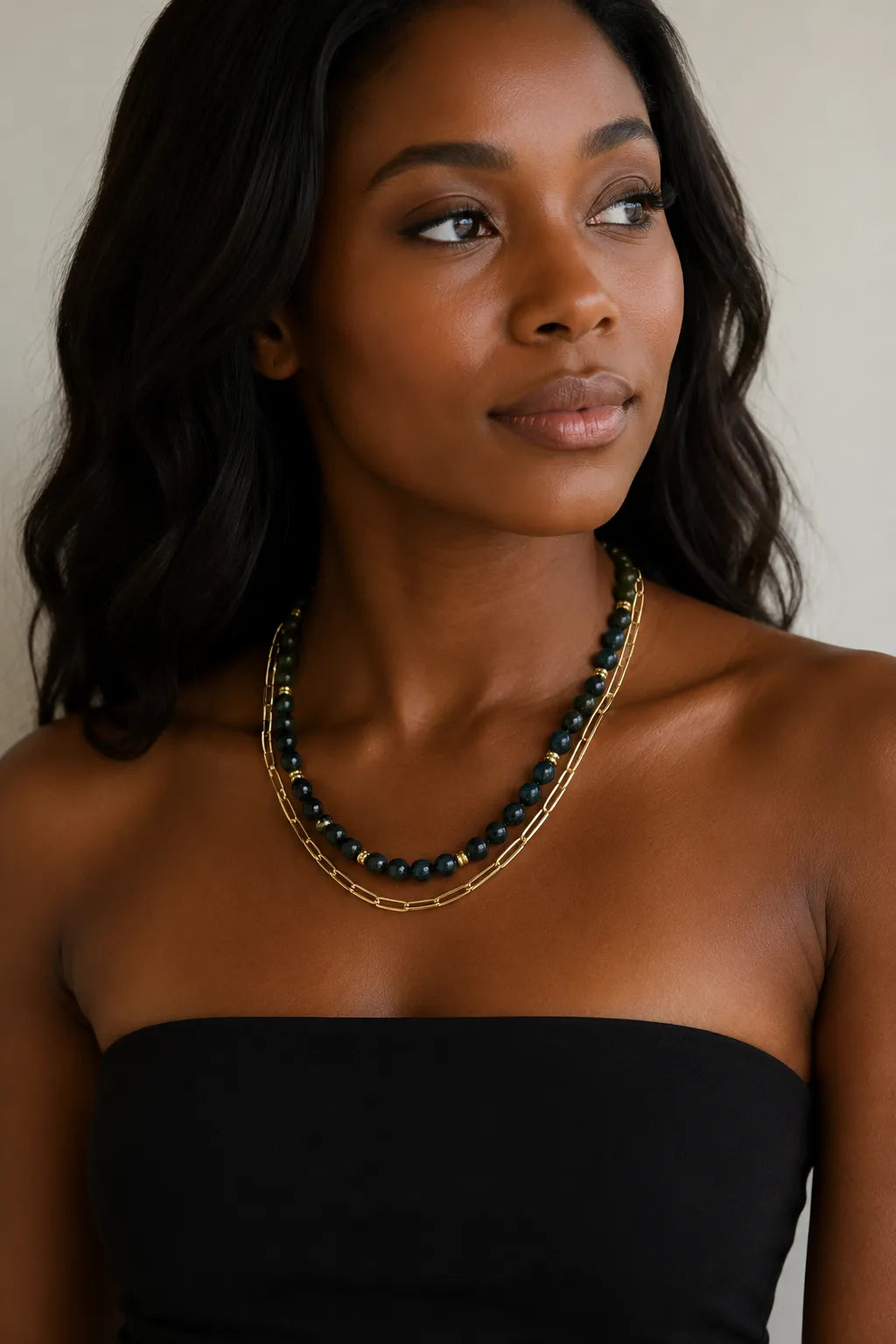A woman wearing layered necklaces by MariaRyan Jewelry. One has ronud dark teal apitie beads and the other has gold paperclip links.