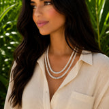 Woman with dark hair wearing layered spiny oyster necklaces and a linen top